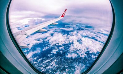 Wide angle of rocky ground through cloudy sky and plane wing from window of aircraft