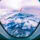 Wide angle of rocky ground through cloudy sky and plane wing from window of aircraft